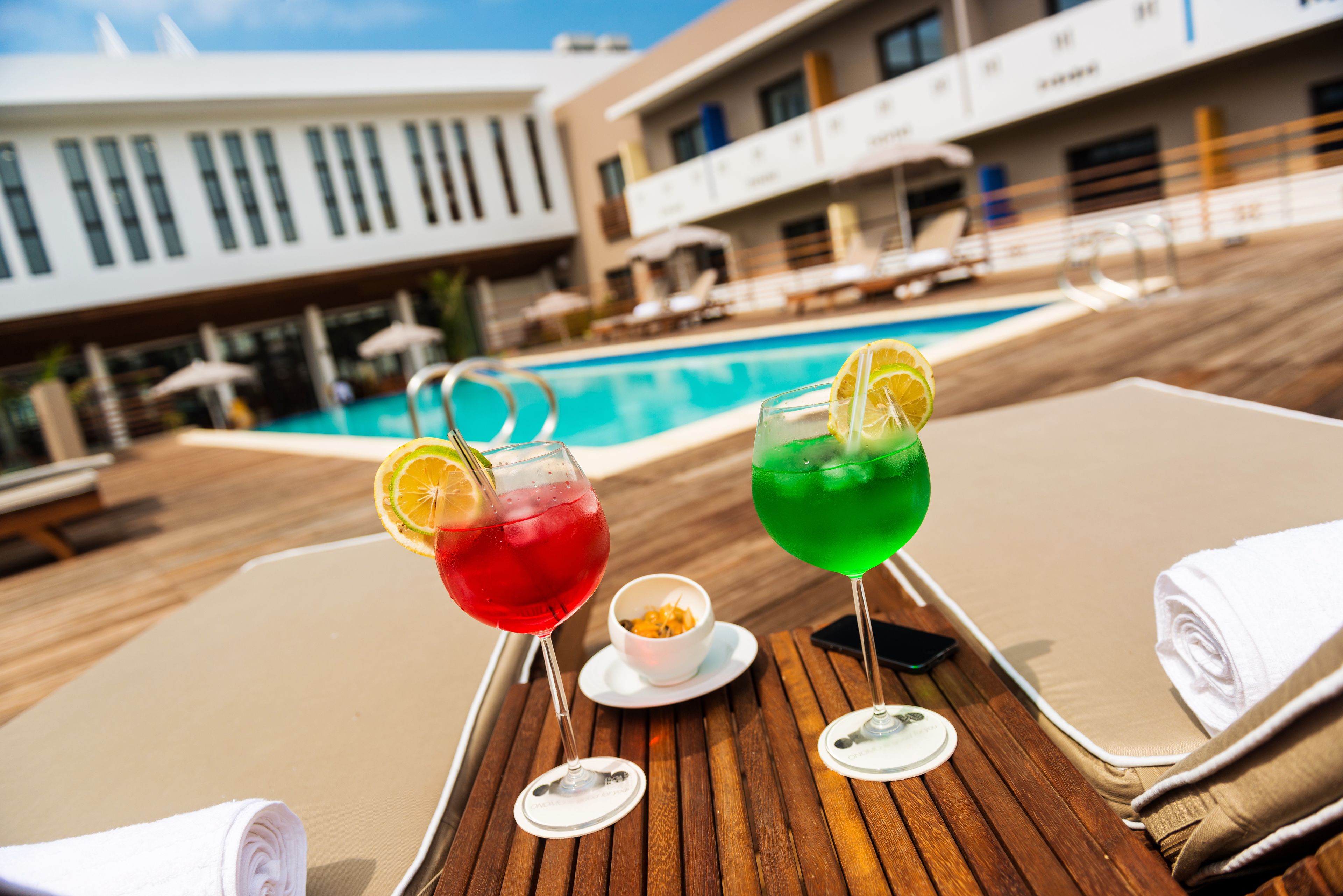 Una mesa junto a la piscina con dos bebidas, un bol de aperitivos y toallas.