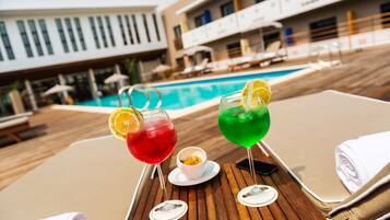 Una mesa junto a la piscina con dos bebidas, un bol de aperitivos y toallas.
