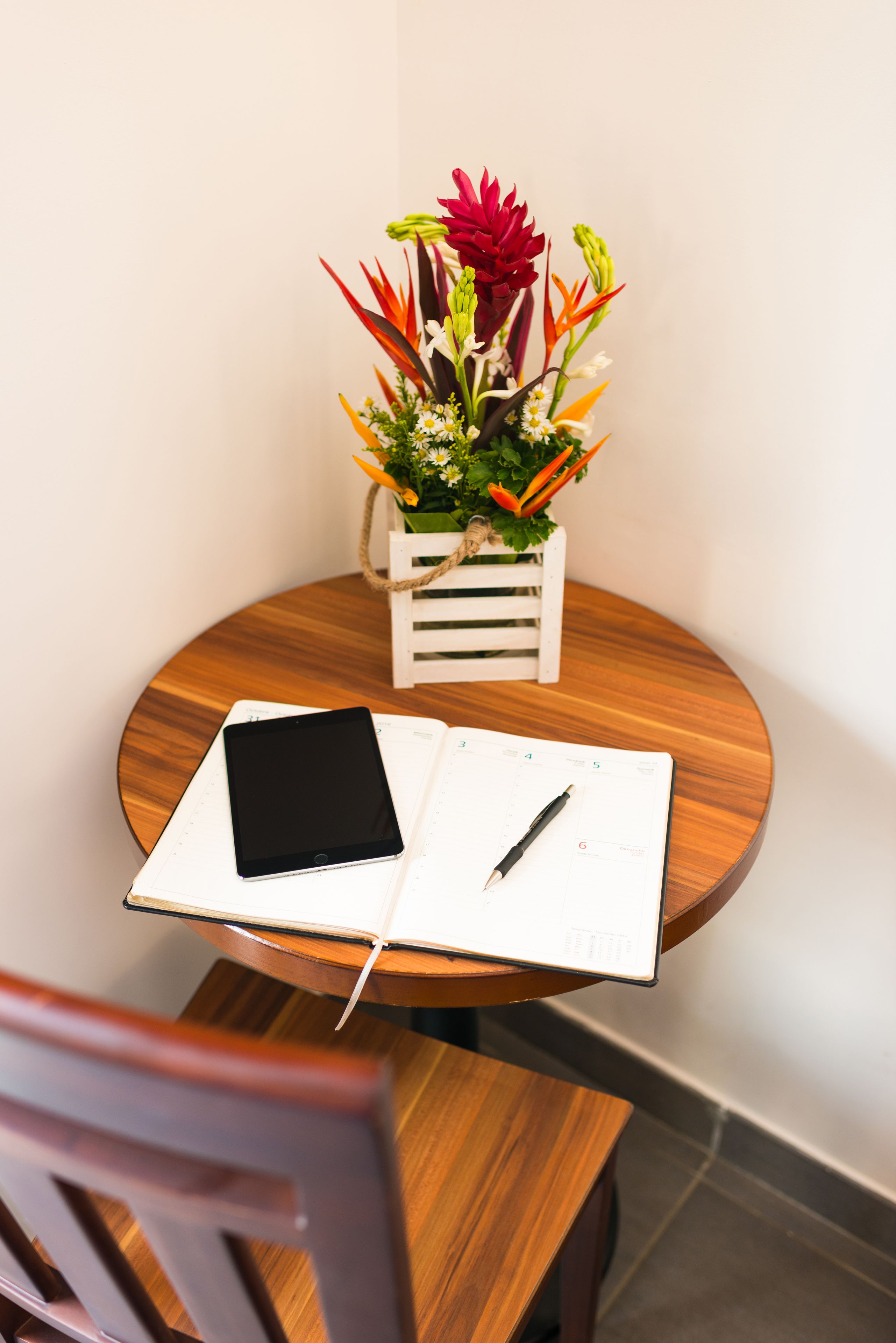 Una mesa de madera con un cuaderno, un bolígrafo y una tableta. Una caja blanca con un arreglo floral está sobre la mesa.