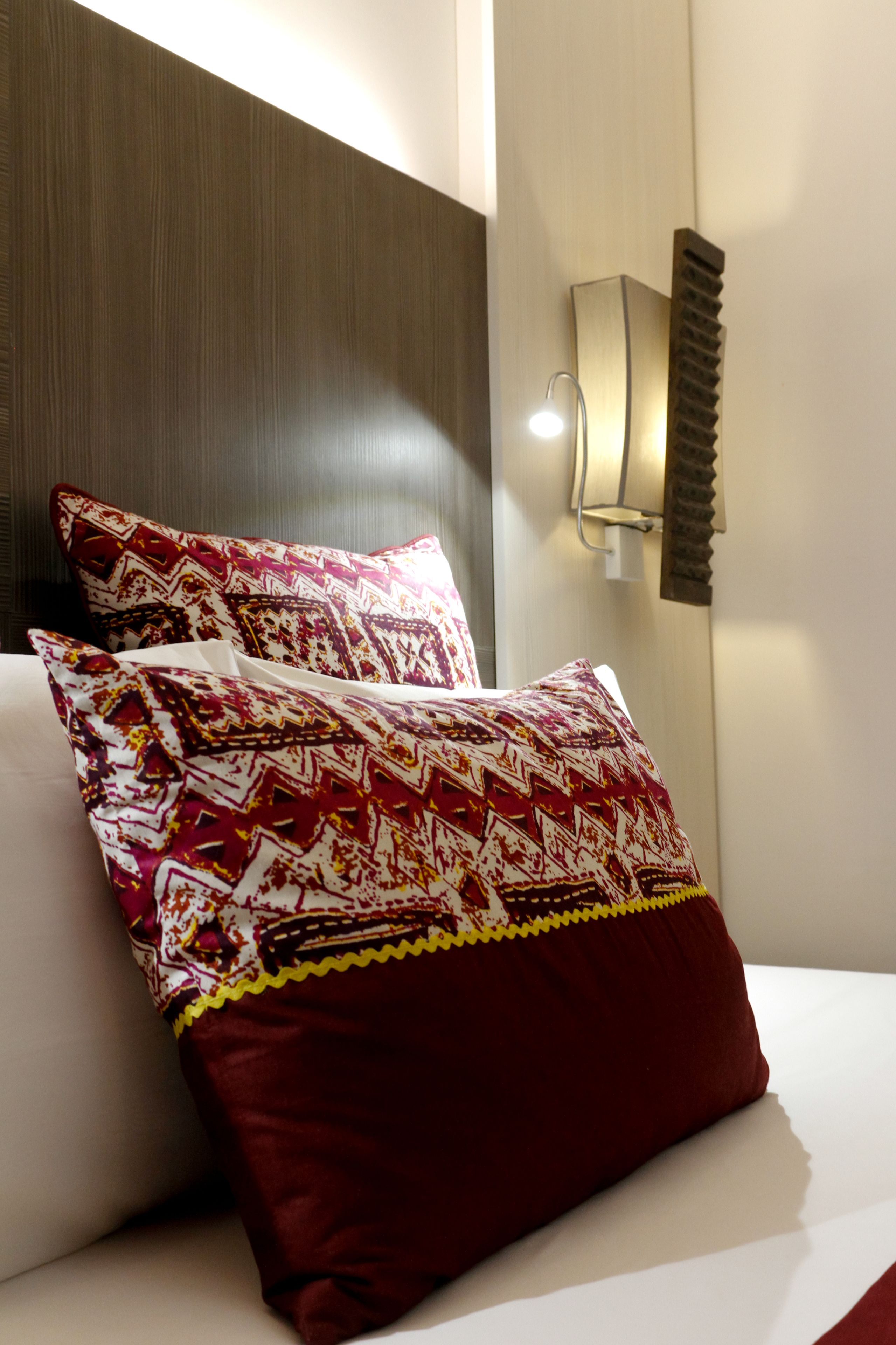 A neatly made bed with patterned pillows and a wall-mounted light fixture.
