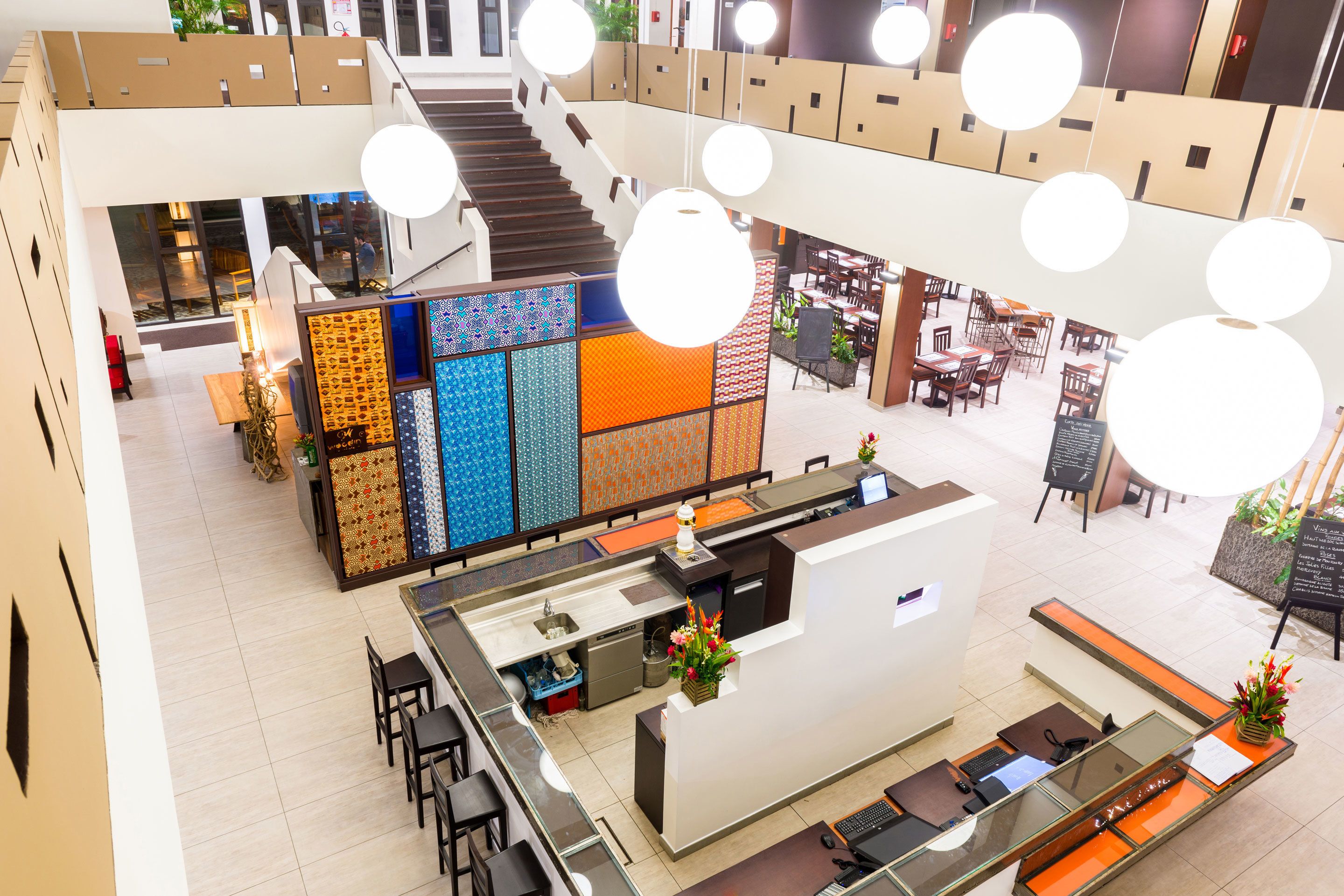A modern hotel lobby with a central reception desk, seating areas, and a staircase leading to upper floors.