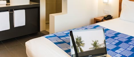 A hotel room with a bed, a laptop, a sink, and a mirror.