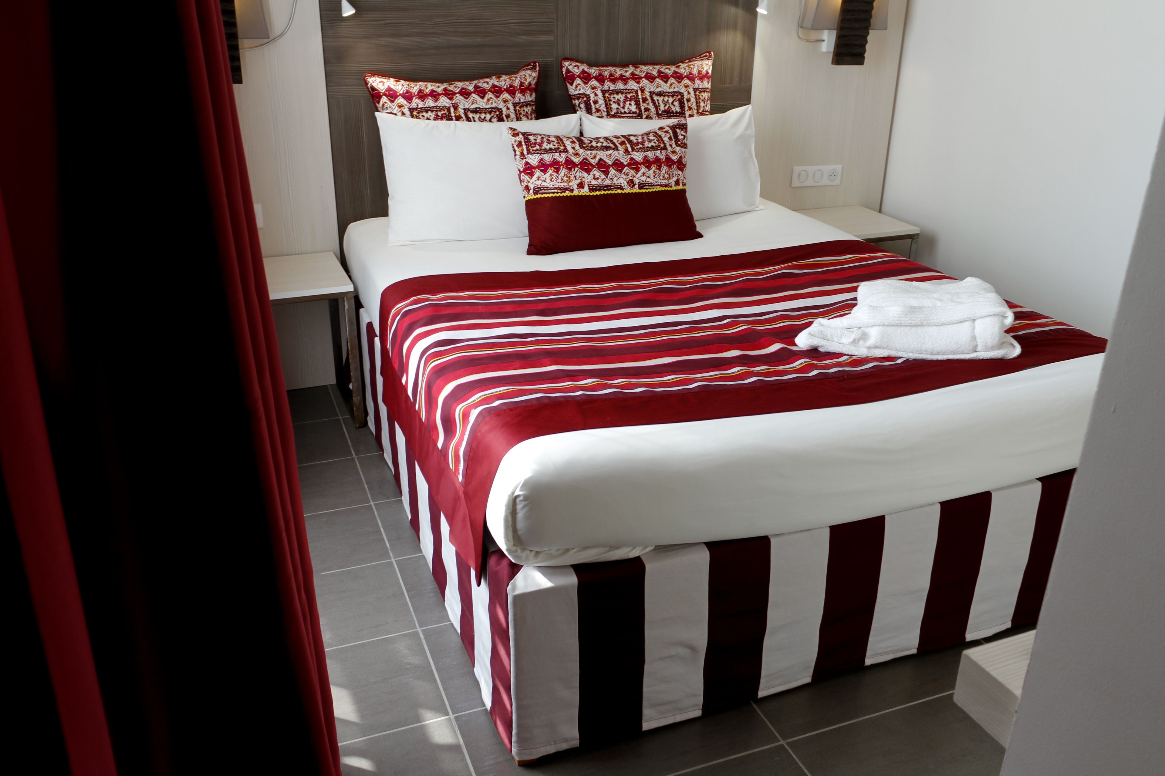 A hotel room with a neatly made bed, a bedside table, and a nightstand.