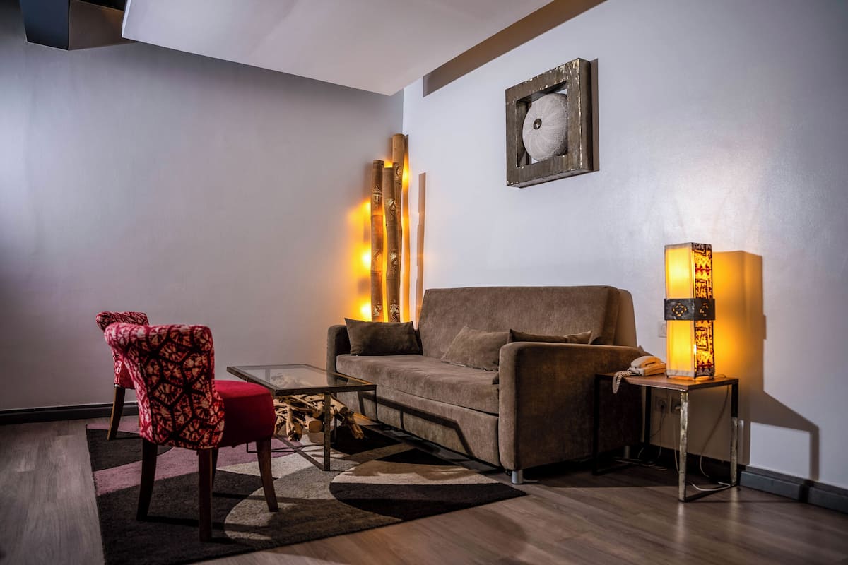Un salon moderne comprenant un canapé, un fauteuil à motifs, une table basse en verre et une table d’appoint avec une lampe.