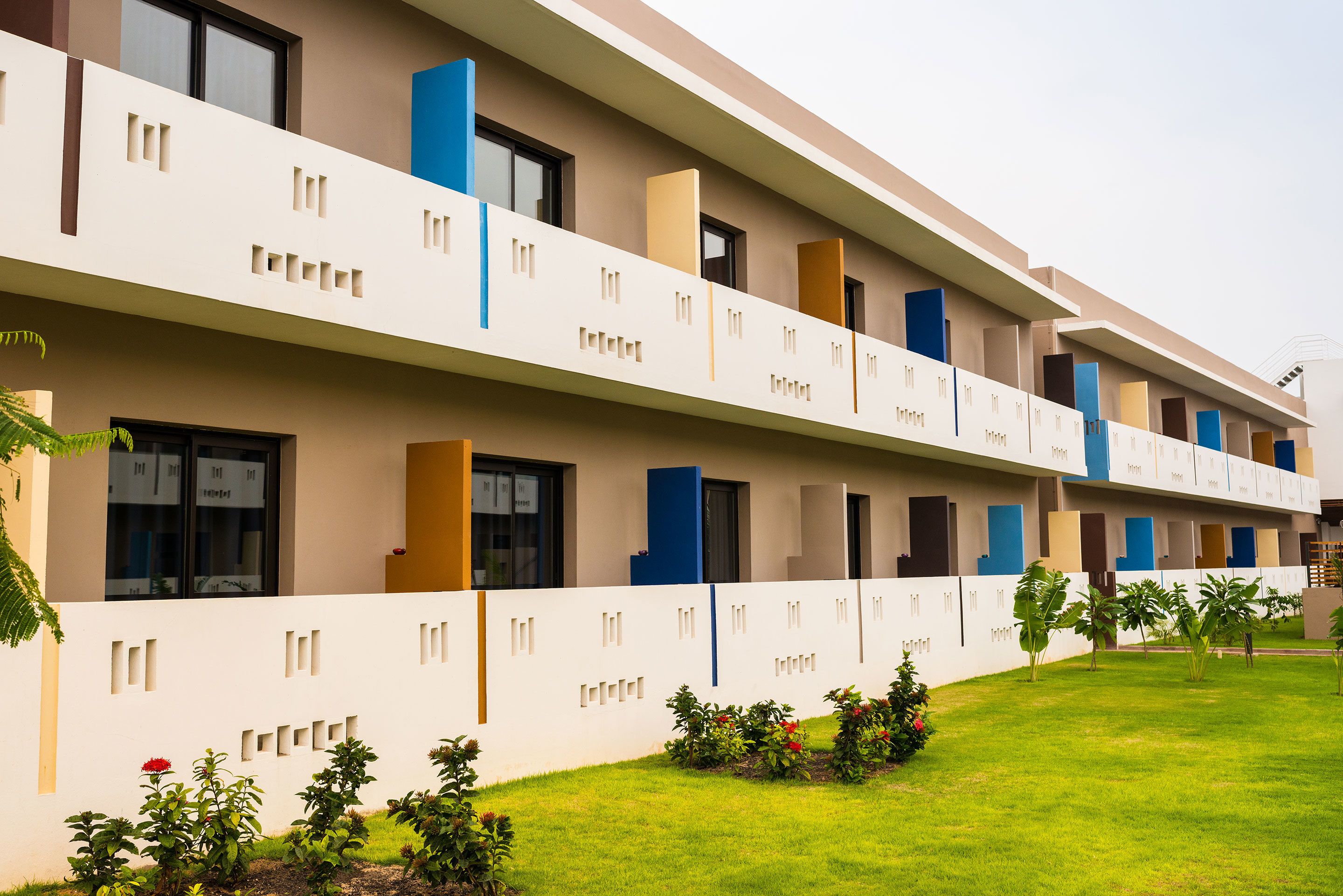 A modern hotel with a flat roof, multiple balconies, and a well-maintained lawn.