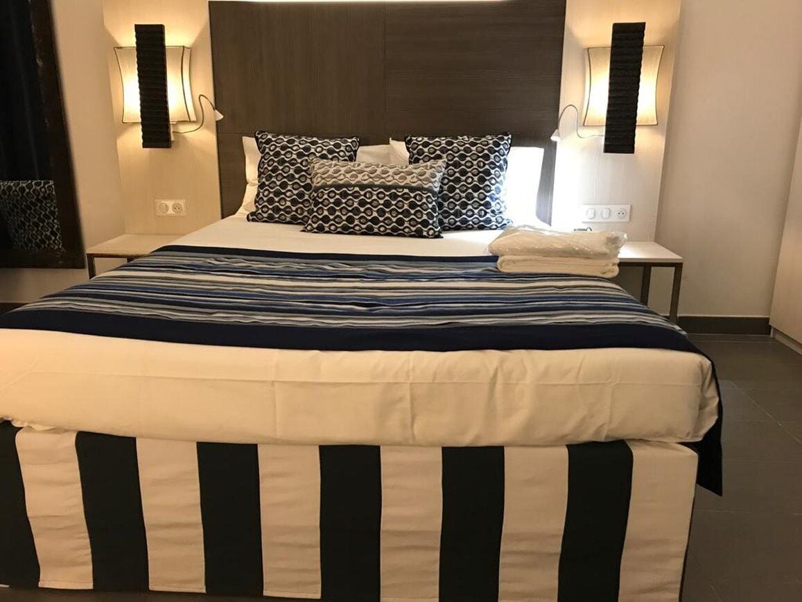 Una habitación de hotel con una cama grande, dos mesitas de noche y lámparas fijadas a la pared.