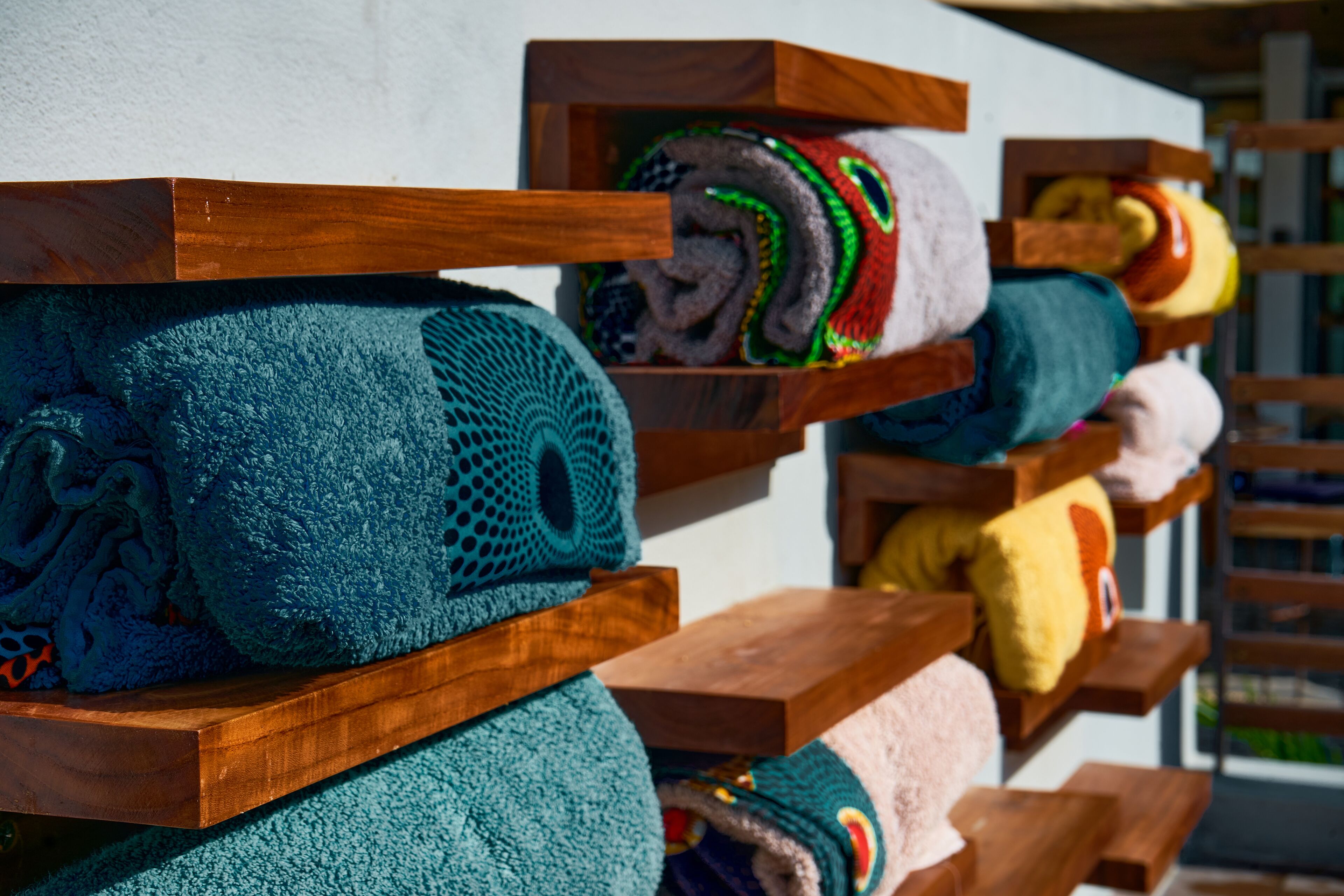 A row of wooden shelves holding rolled-up towels in various colors.