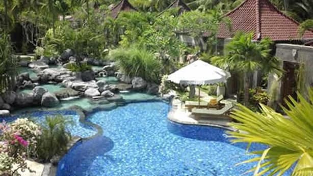 A large outdoor swimming pool surrounded by rocks and greenery, with a gazebo and lounge area. - Parigata Villas Resort (Denpasar)