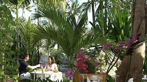 An outdoor dining area with tables and chairs, surrounded by lush greenery and flowering plants. - Parigata Villas Resort (Denpasar)