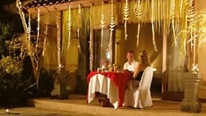 A dining area with a table set for two, a pool in the foreground, and decorative elements hanging above. - Parigata Villas Resort (Denpasar)