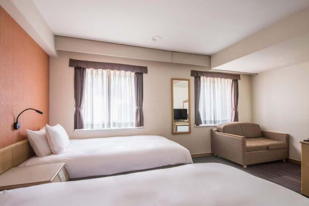 A hotel room with two beds, a chair, a desk, and a mirror.