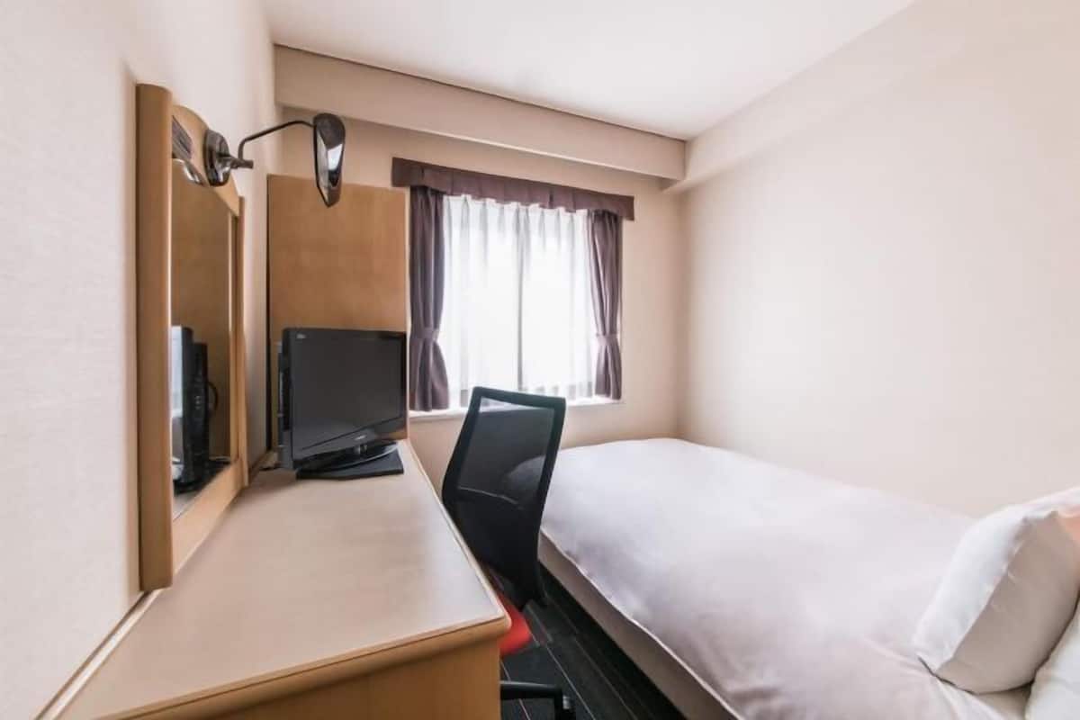 A hotel room with a bed, a desk with a chair, a television, and a window with curtains.