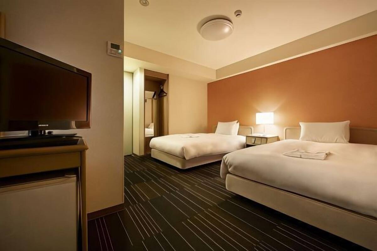 A hotel room with two beds, a TV, a desk, and a mirror.