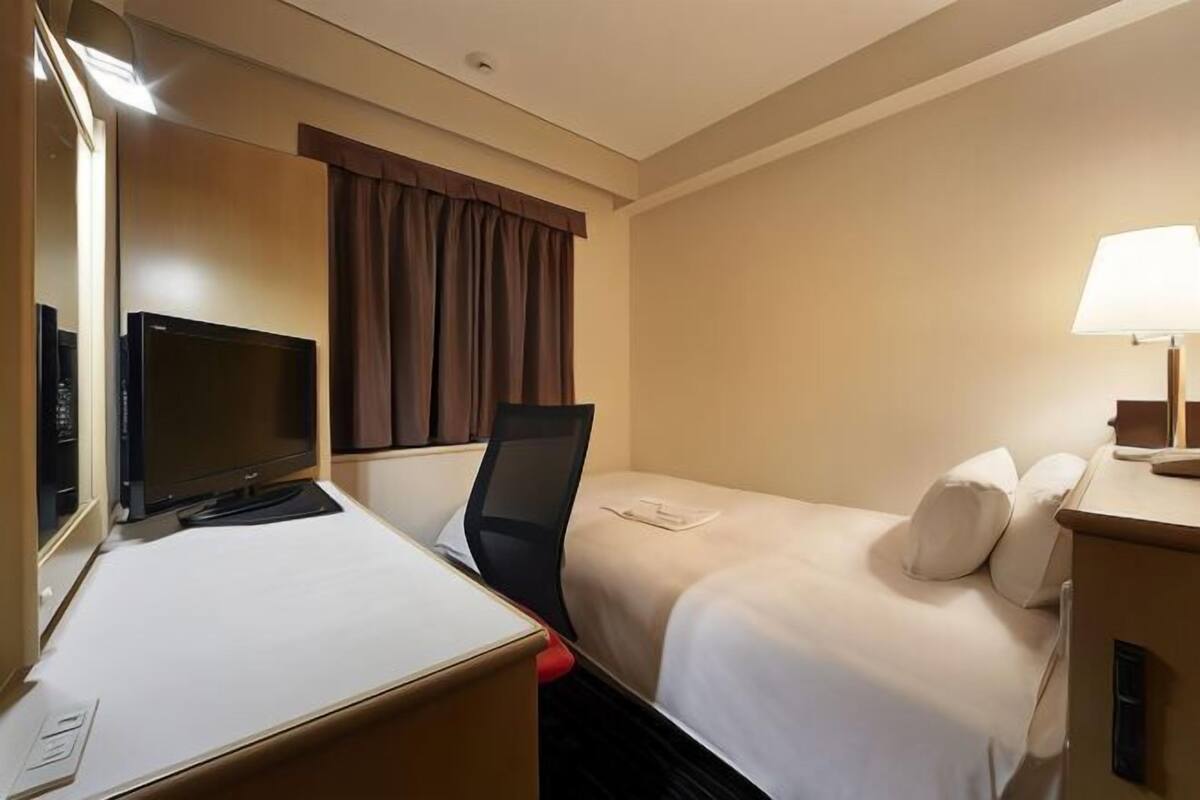 A hotel room with a bed, a desk with a computer, a TV, and a lamp.