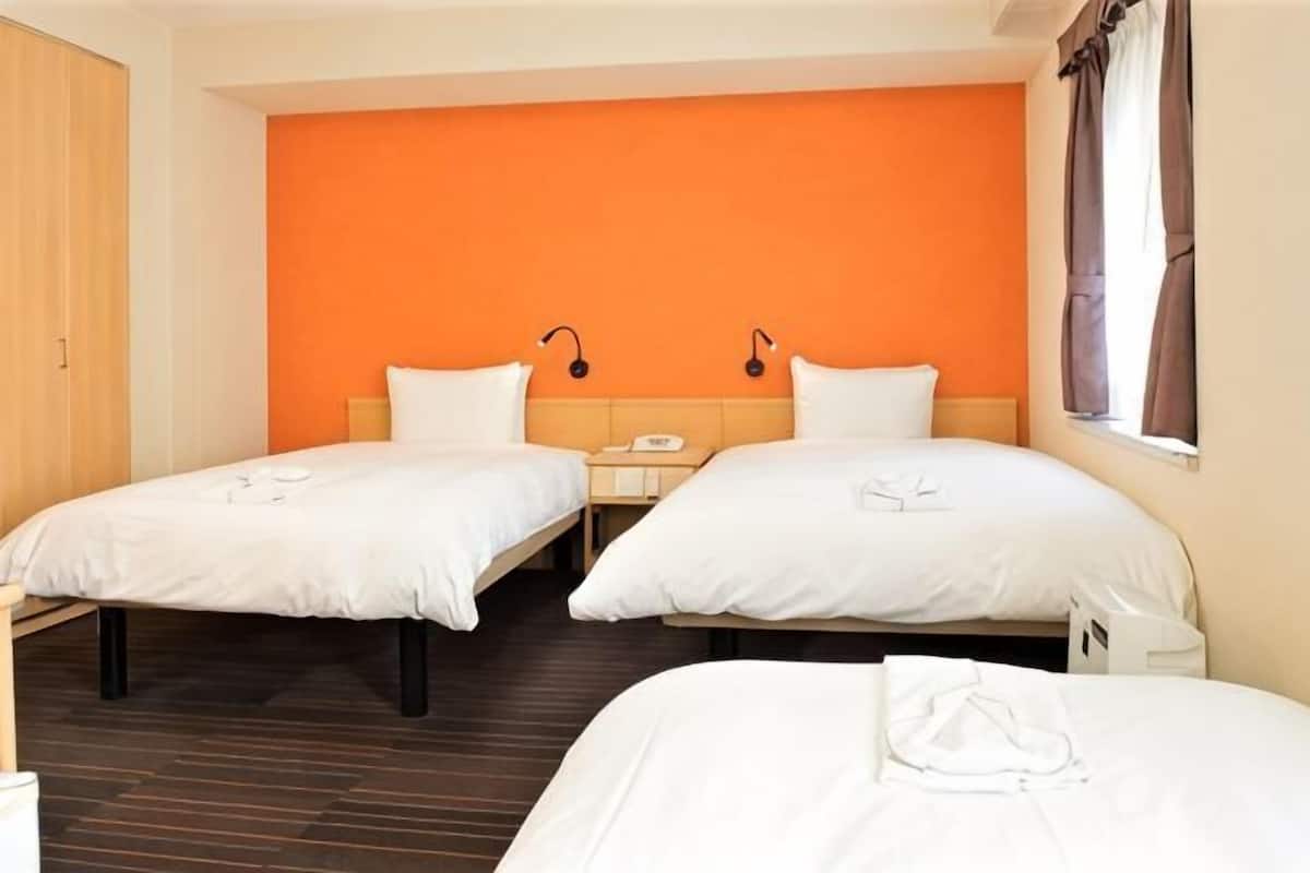 A hotel room with two beds, a wooden wardrobe, a nightstand, and a window with curtains.