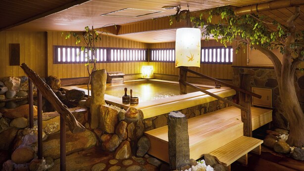 Uma onsen japonesa tradicional com interiores de madeira, degraus de pedra e um banco de madeira.