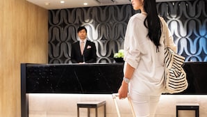 Uma área de recepção de hotel com design moderno, destacando um balcão de mármore e uma parede com padrão.