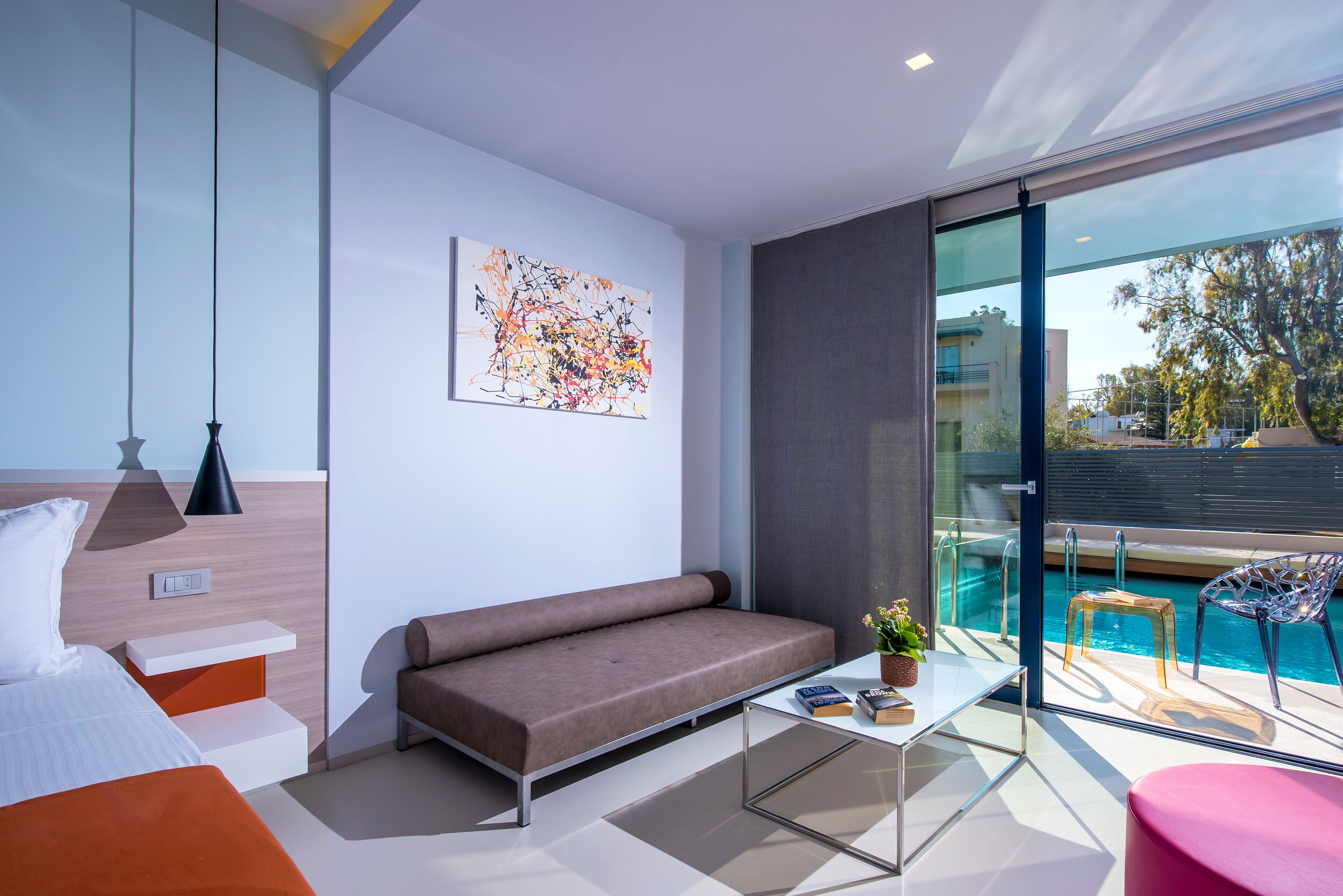 A modern hotel room with a sofa, a glass coffee table, a bed, and a view of a swimming pool.