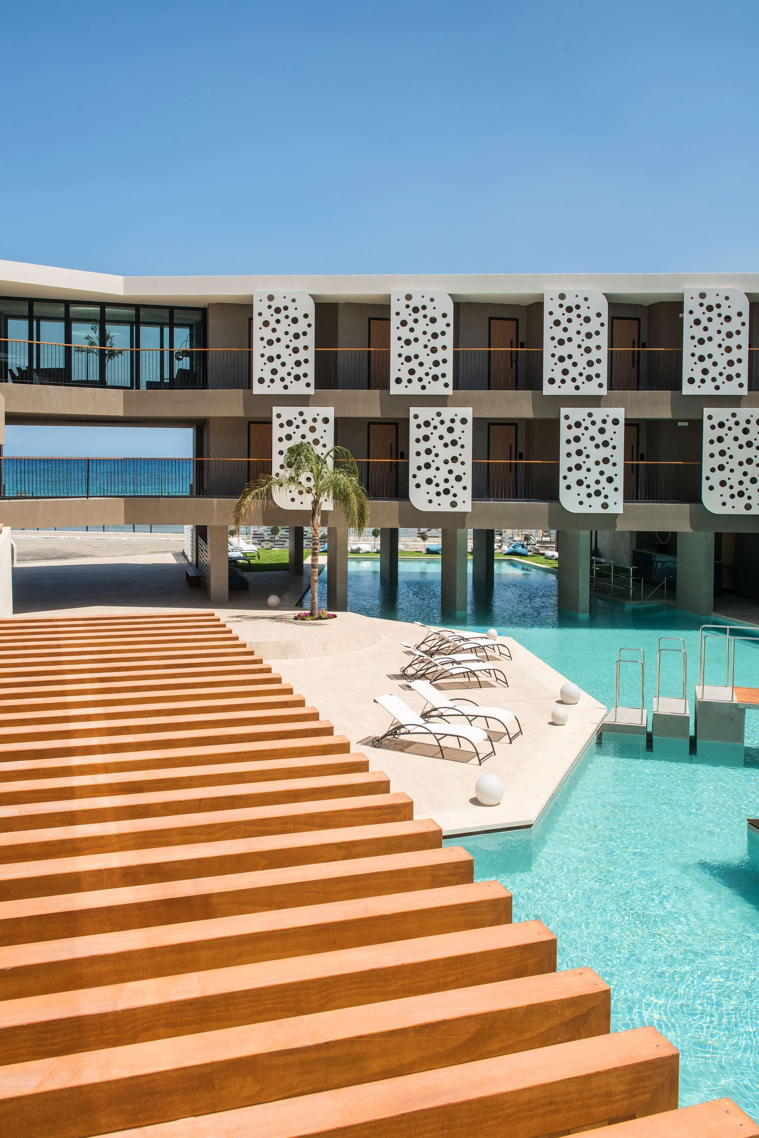 A hotel with a pool, wooden steps, and a view of the ocean.