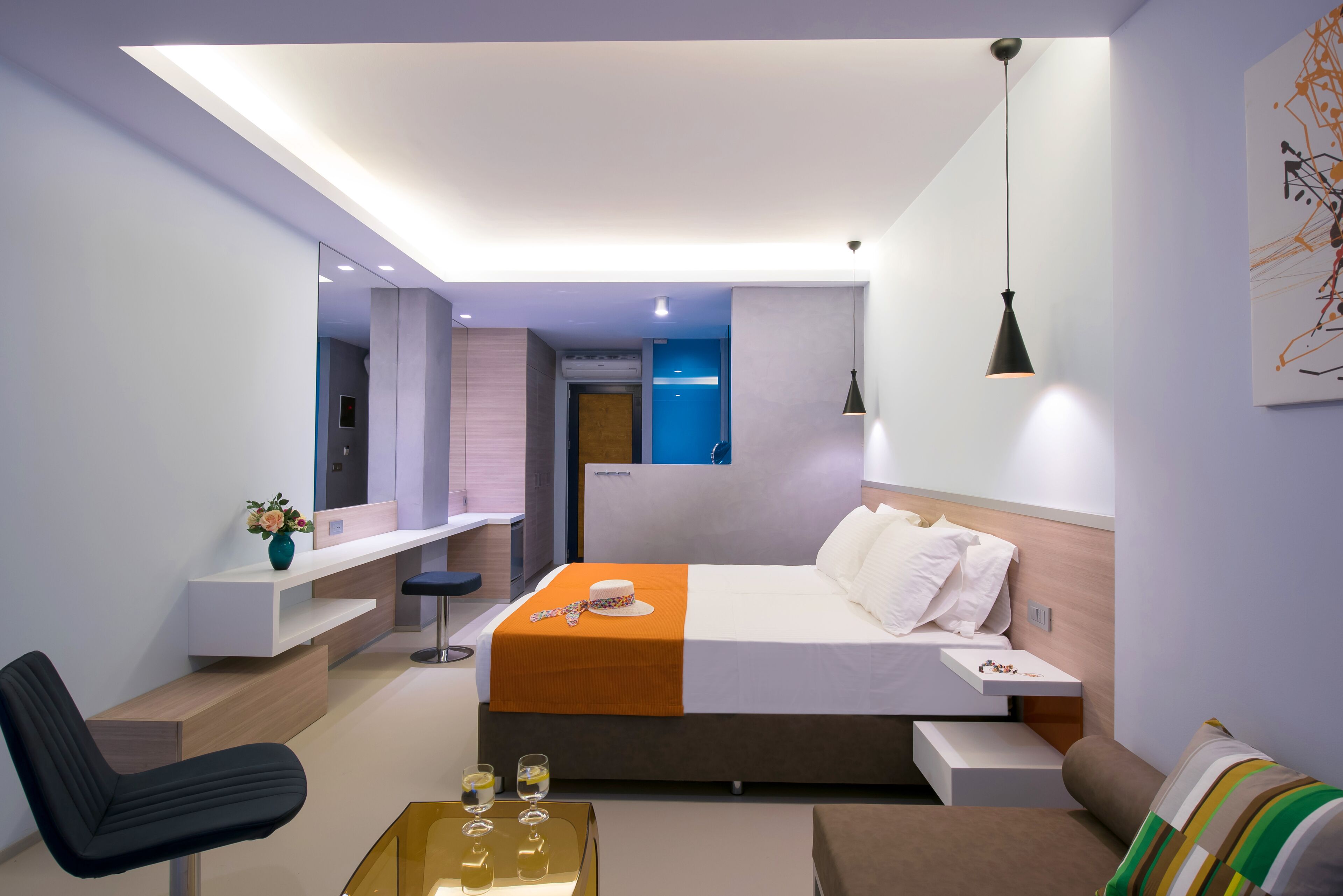 Een moderne hotelkamer met een bed, nachtkastje, bureau, stoel, bank en een klein bijzettafeltje.