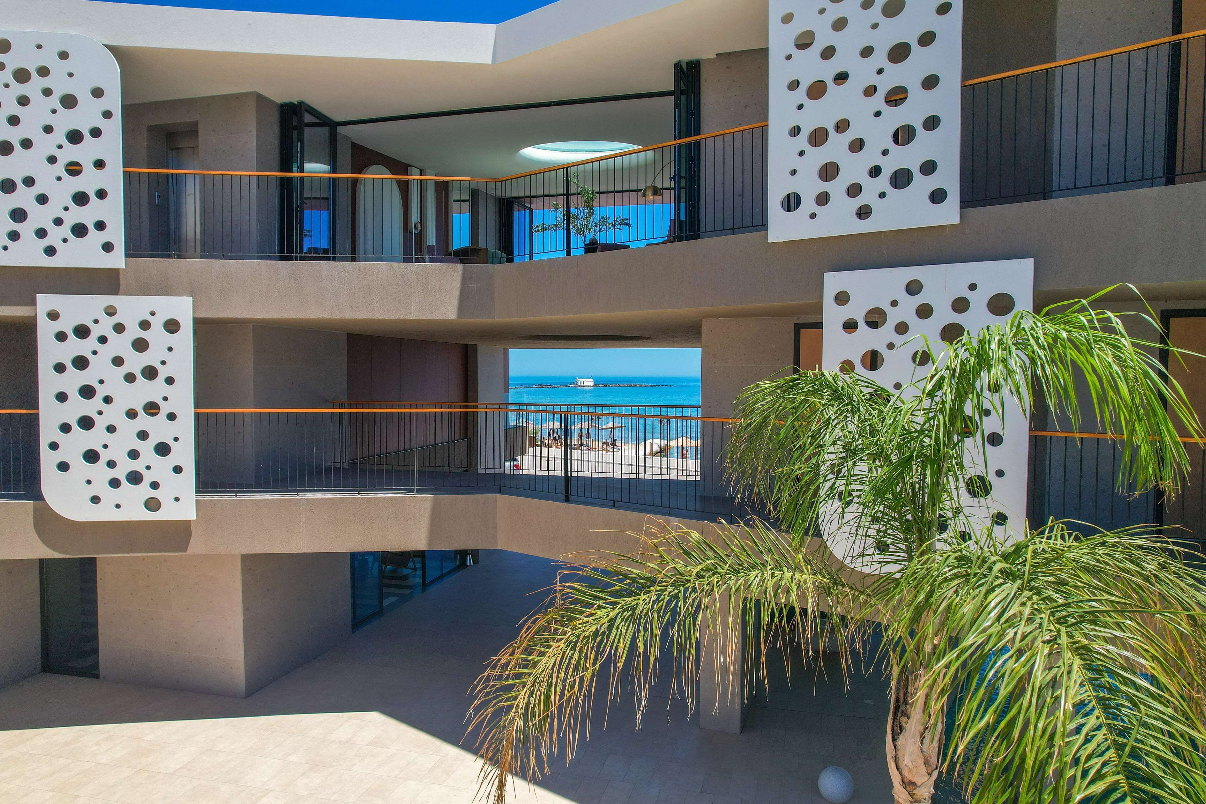 Un hôtel à plusieurs étages doté de balcons, offrant une vue sur la mer et bordé de palmiers.