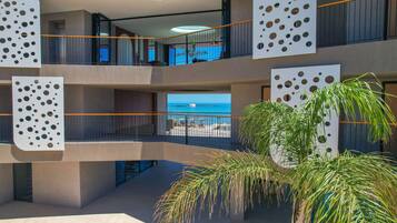 Un hôtel à plusieurs étages doté de balcons, offrant une vue sur la mer et bordé de palmiers.