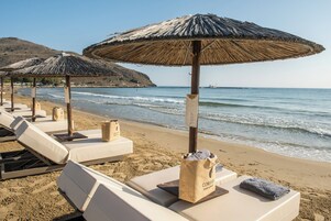 Un hotel frente a la playa con tumbonas, sombrillas de paja y vista al mar.