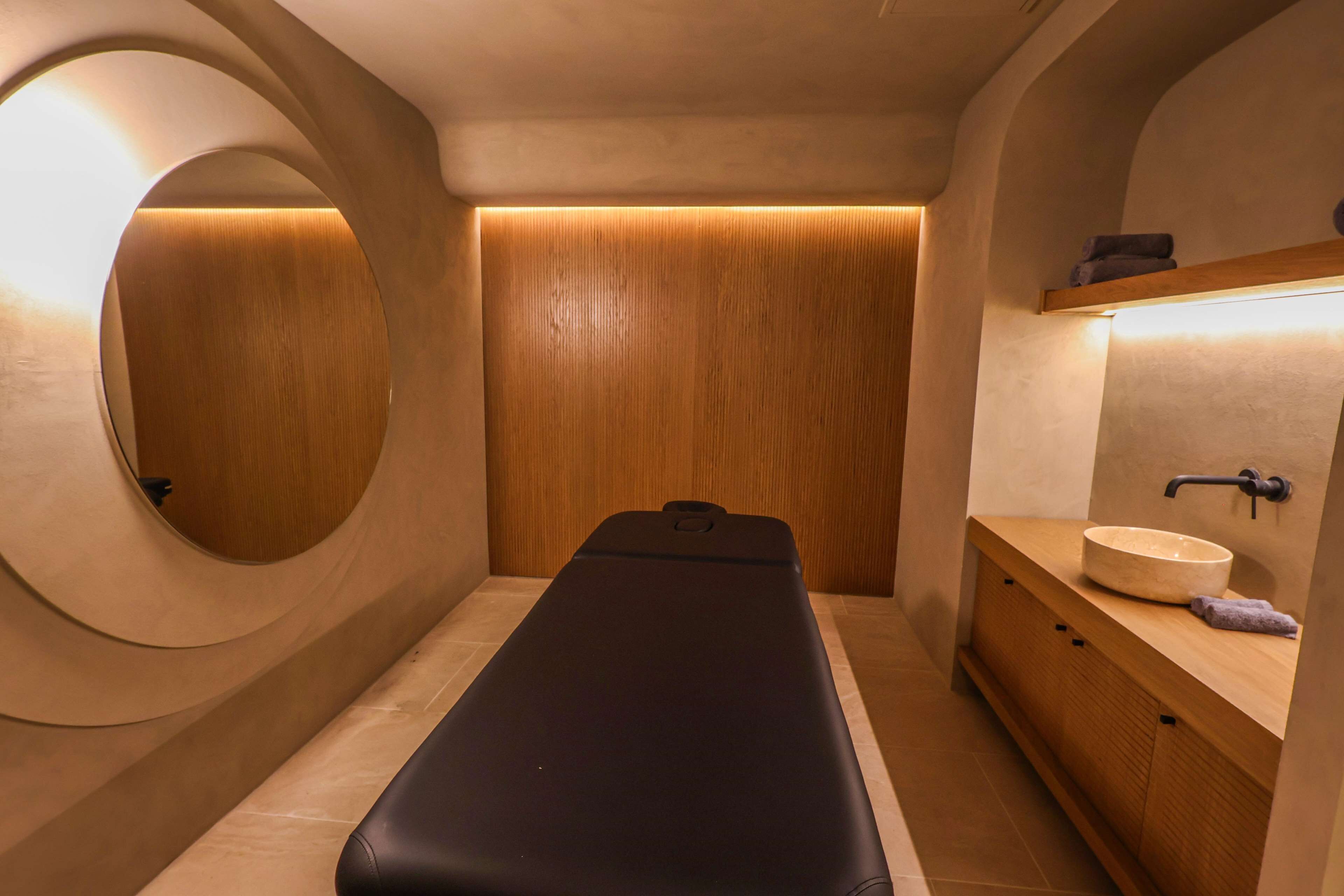 Et moderne badeværelse med et trækommode, et rundt spejl og et massagébord.