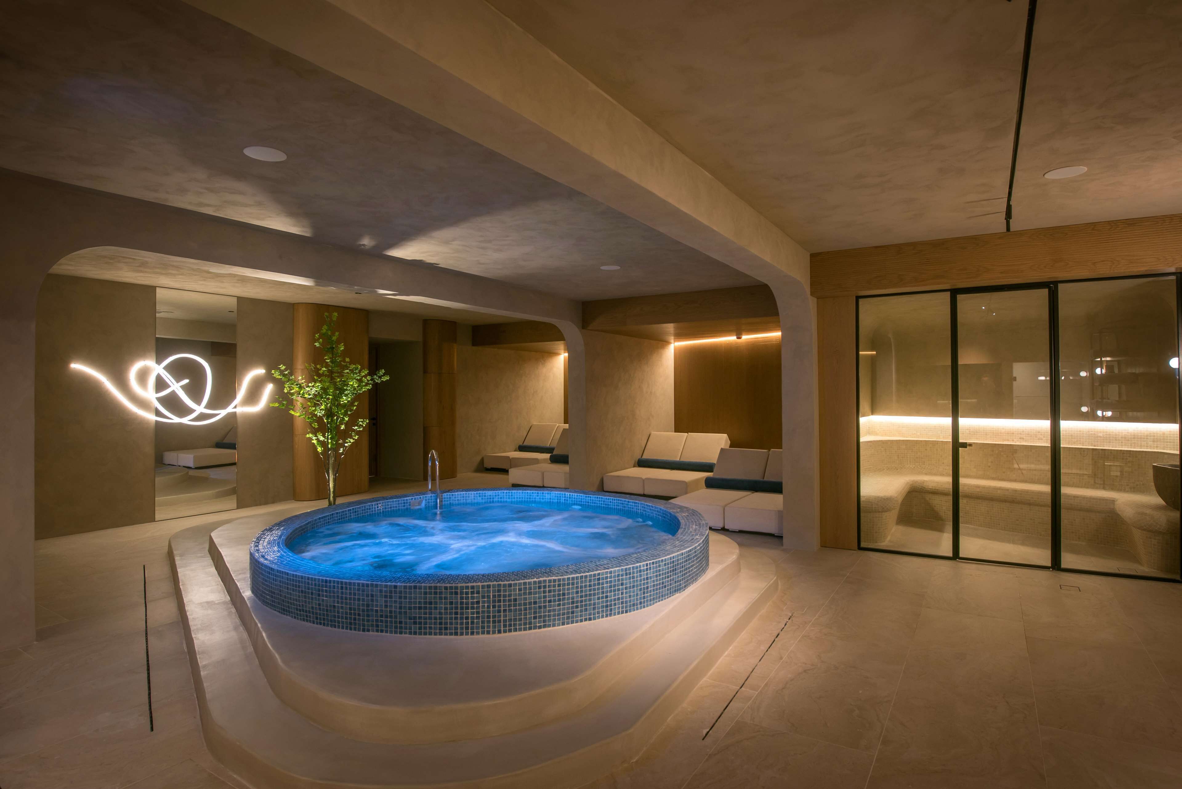 A modern spa area with a hot tub, seating, and a glass partition.