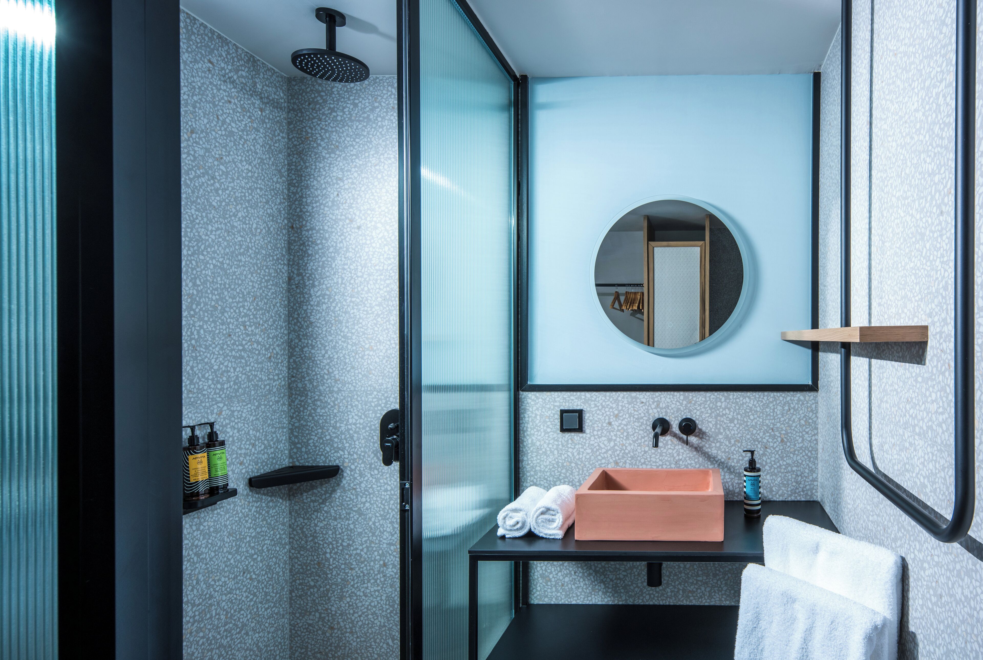Ein modernes Badezimmer mit Duschabtrennung aus Glas, einem schwarzen Waschbecken mit rosa Becken und einem runden Spiegel darüber.