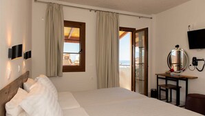 Habitación de hotel con cama, escritorio con espejo, televisor y vista al mar a través de una ventana.