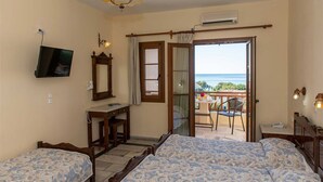 Un dormitorio con dos camas, televisión, escritorio y balcón con vista al mar.