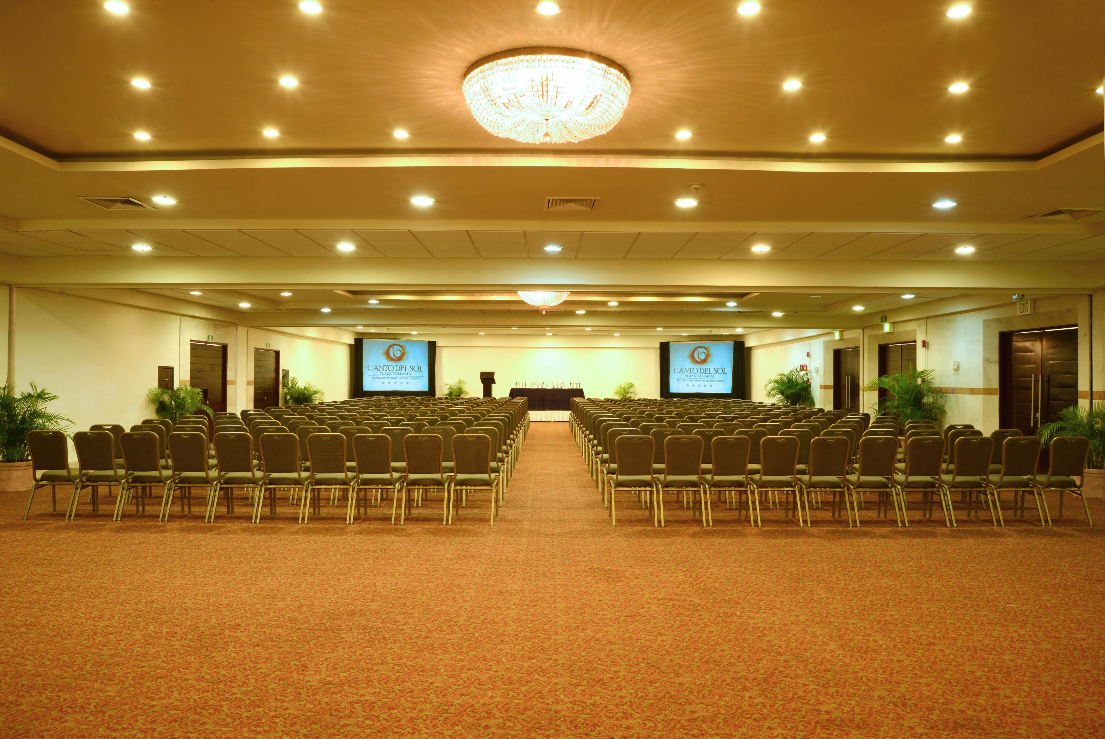 Un salón de conferencias con filas de sillas, un escenario y una gran lámpara de araña.