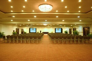 Un salón de conferencias con filas de sillas, un escenario y una gran lámpara de araña.
