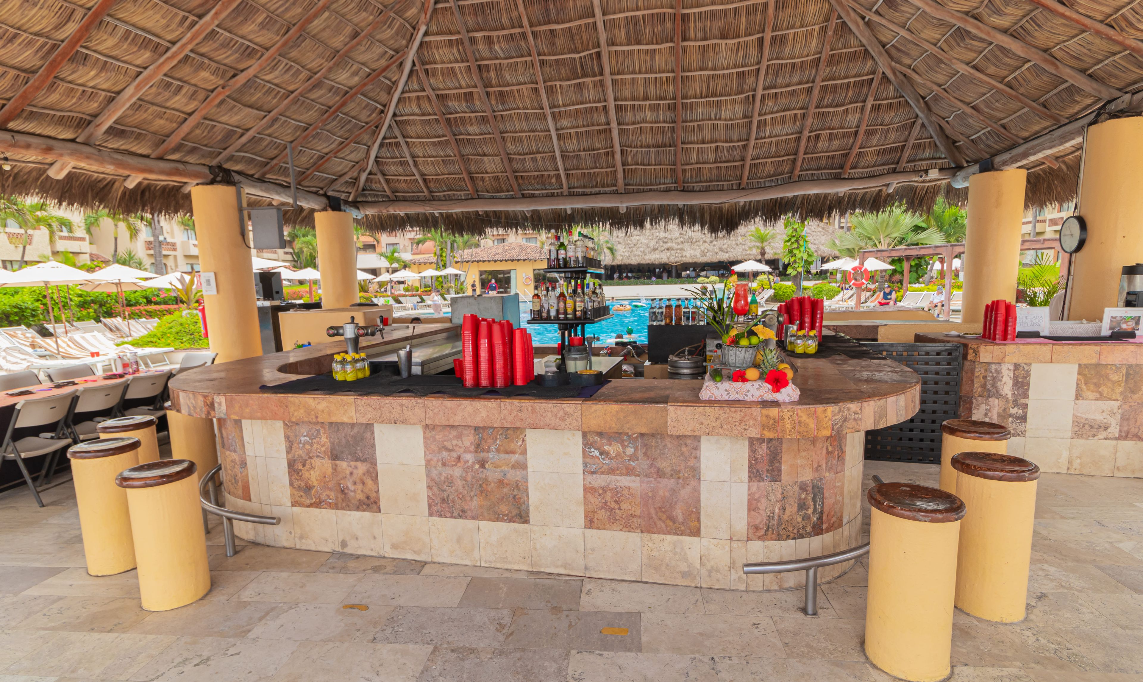 Eine Bar mit Pool im Hintergrund, umgeben von Liegestühlen und Sonnenschirmen.