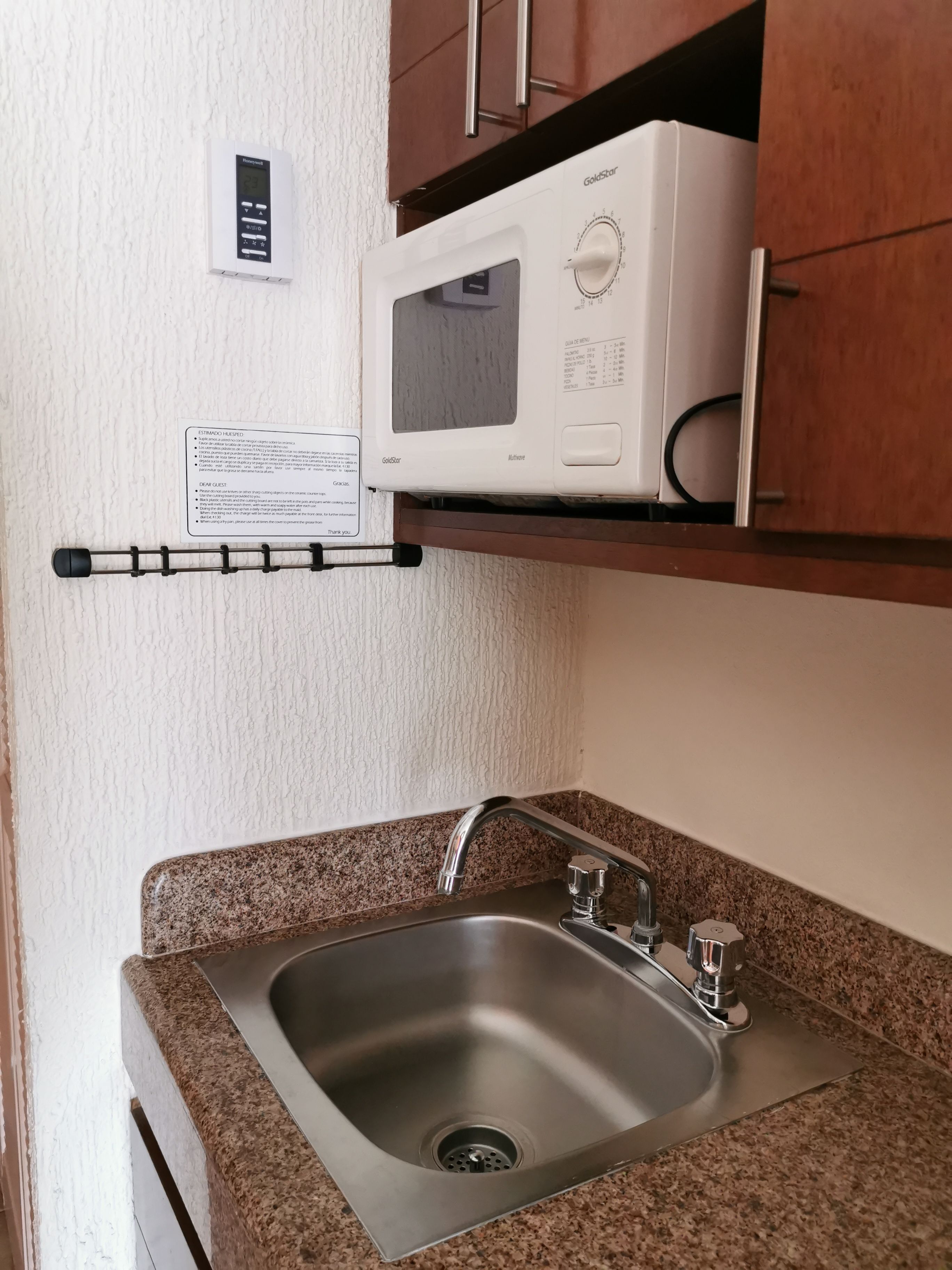 Una cocina con un lavamanos de acero inoxidable, un microondas y un termostato instalado en la pared.