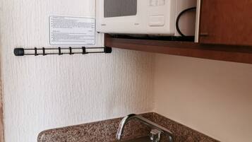 Una cocina con un lavamanos de acero inoxidable, un microondas y un termostato instalado en la pared.