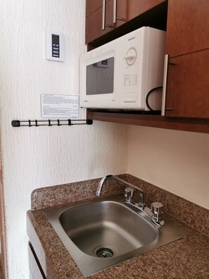 Une cuisine équipée d’un évier en acier inoxydable, d’un four à micro-ondes et d’un thermostat fixé au mur.