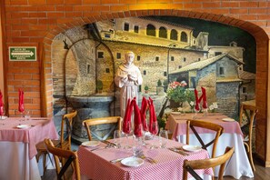 Een restaurantinterieur met stenen muurschilderingen, rode en witte geruit tafelkleden, en een standbeeld.