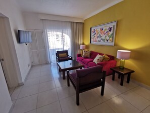 Una sala de estar con un sofá, sillones, una mesa de centro, un televisor y un cuadro en la pared.
