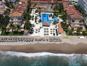 Luchtbeeld van een resort met een centraal zwembad, diverse loungeruimtes en een strand.