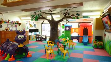 Un área de juegos infantiles con una gran estructura de árbol, alfombras de colores y diverso mobiliario de juego.