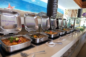Een buffet met diverse gerechtopties, inclusief containers met labels voor de verschillende gerechten.