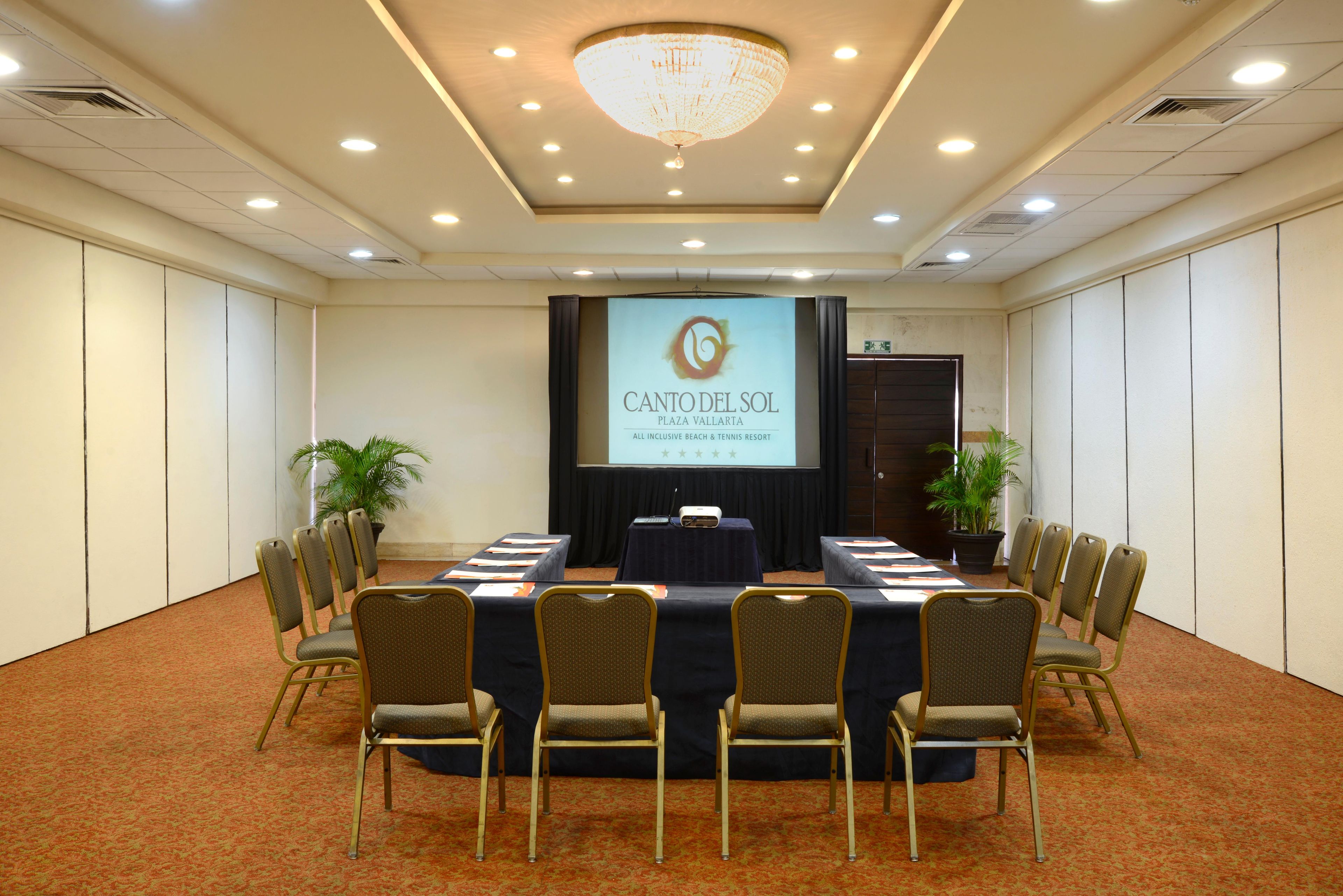 A conference room with a long table, chairs, a projector screen, and a chandelier.