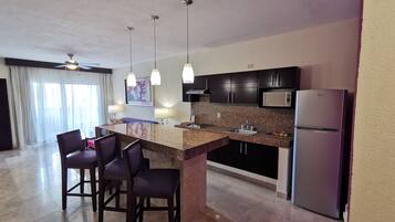 A modern kitchen with a granite countertop, dark cabinets, a stainless steel refrigerator, and pendant lighting.