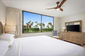 A hotel room with a large bed, a television, a wooden dresser, and a view of palm trees.