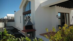 Une maison moderne dotée d’une grande cheminée, d’un chemin de pierre et d’un petit jardin.