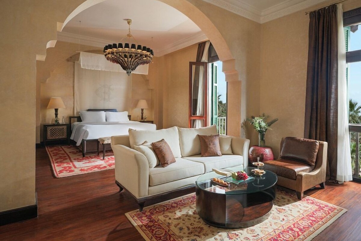 A hotel room with a sofa, armchair, coffee table, and a bed with a canopy.