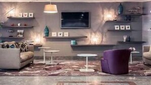A modern living room with a sofa, a purple armchair, a coffee table, a TV, and shelves with decorative items. - Hôtel Mercure Marseille Centre Vieux-Port (MARSEILLE)