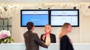 A reception area with a reception desk, two monitors, and a vase of flowers. - Hôtel Mercure Marseille Centre Vieux-Port (MARSEILLE)
